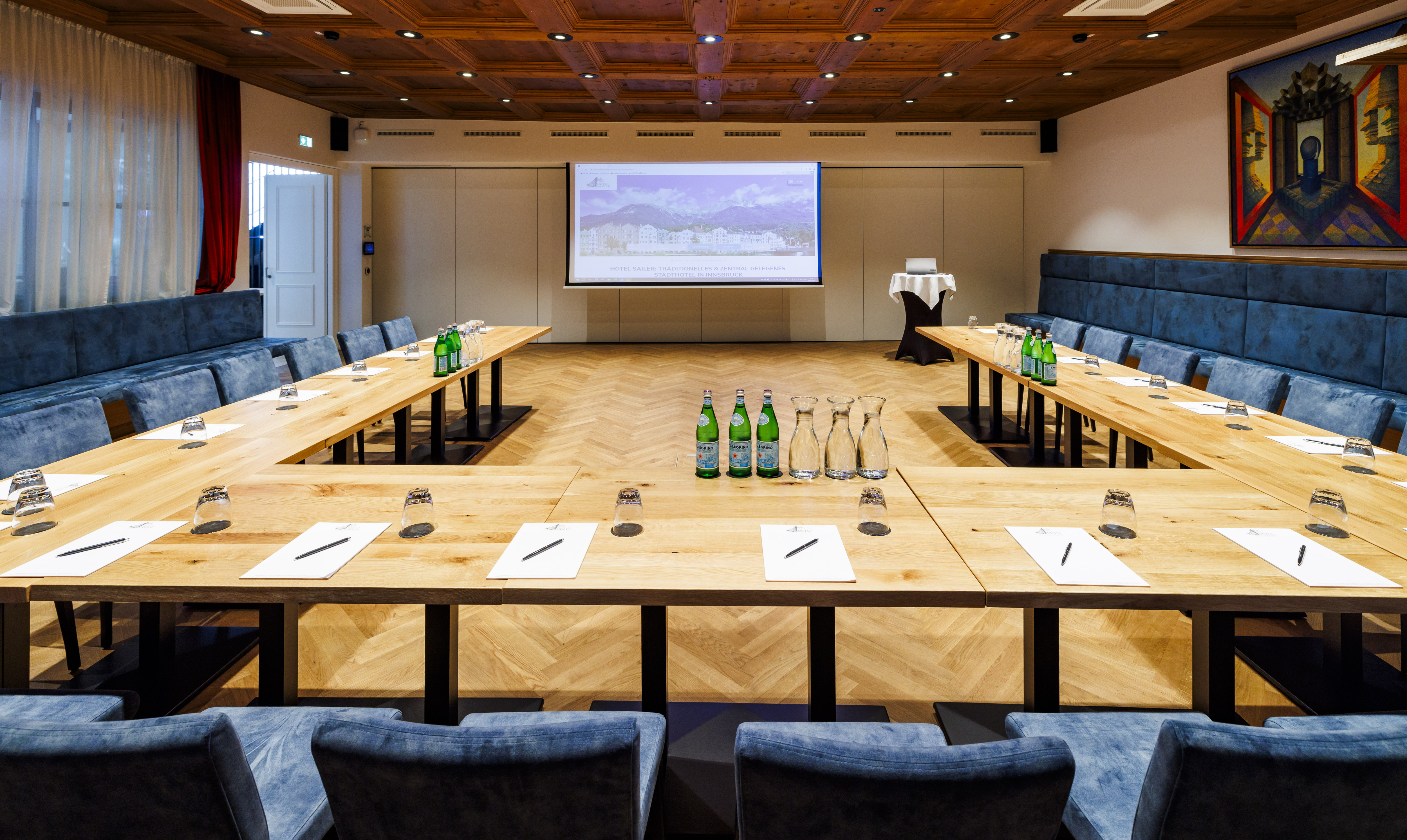 Modern conference room with wooden tables, blue chairs and technical equipment for presentations.